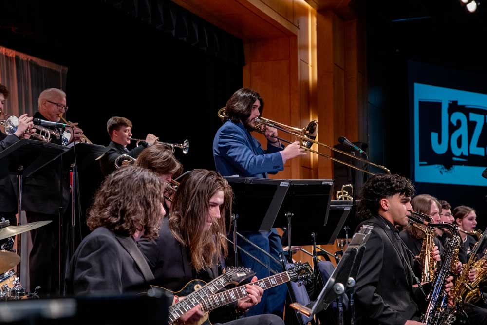 A lively jazz band performing on stage with one musician standing, playing a trombone solo.