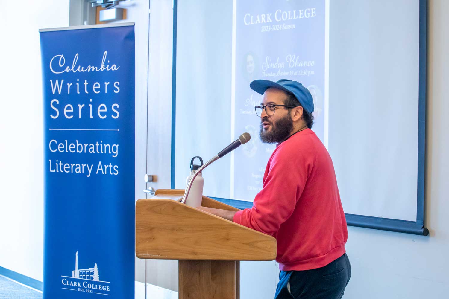 A person speaking at a podium with a microphone, with a banner that says 'Columbia Writer Series: Celebrating Literary Arts' next to them.