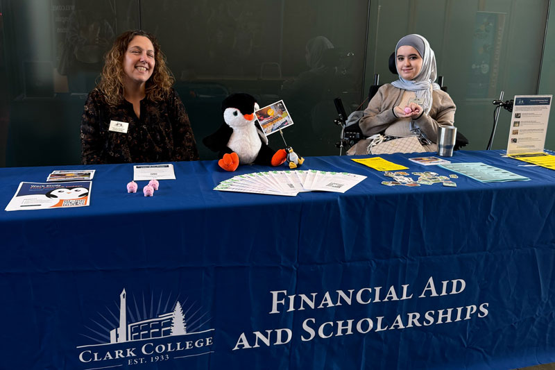 Two people at a table with papers and flyers spread out, with a penguin stuffed animal on the table.