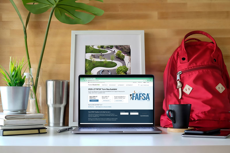 A desk with a laptop displaying the FAFSA page, a backpack on the right, and plants, mugs, and books arranged nearby.