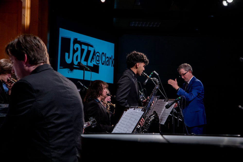 A student performs in front while the conductor directs the assembled ensemble behind them.