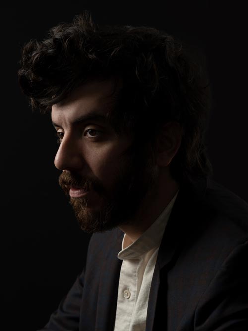 Side profile of poet and novelist Kaveh Akbar against a dark background