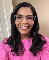 A woman wearing glasses smiles warmly at the camera