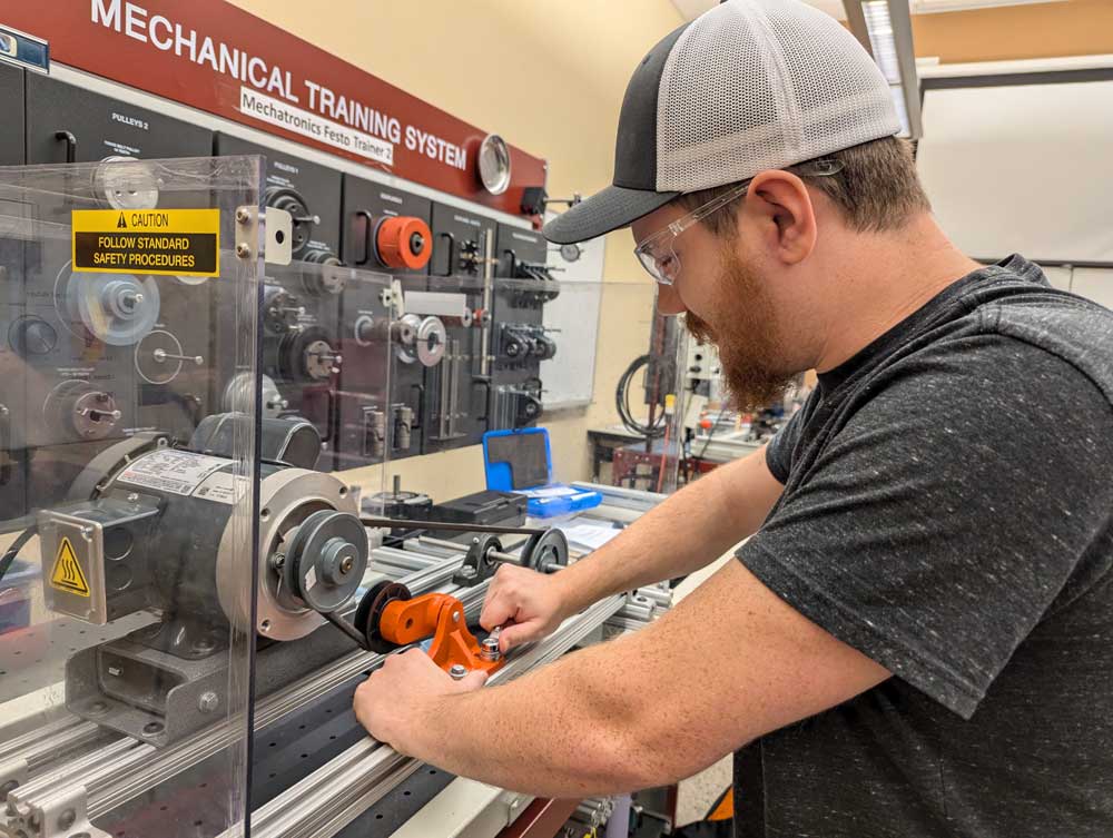 A student works on a mechanical training system in a workshop setting.