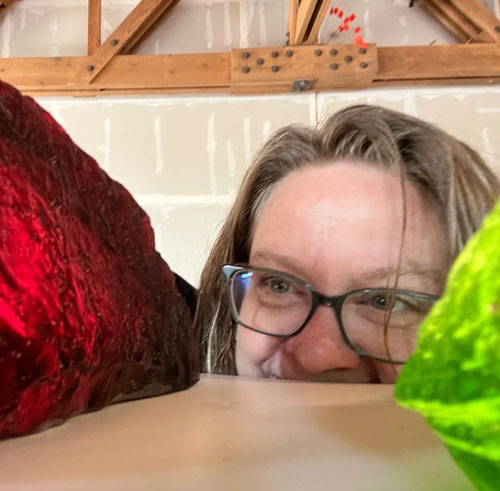 A person wearing glasses peeking out from under a table, gazing at a glowing rock that softly illuminates their face.