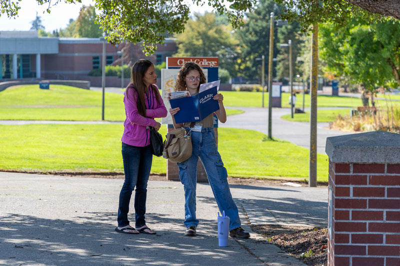 Two people on a college campus look through papers in a folder labeled 'Clark College'.