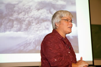 Dr. Charlene Montierth in front of an image of a volcano on a large screen