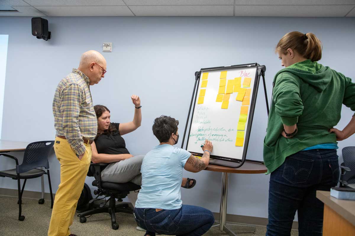 Clark College faculty collaborating around a white board. One person is writing on the board, one person is speaking, and two others look on.